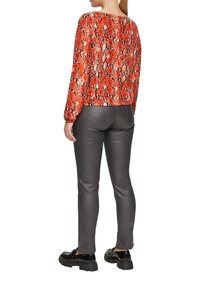 Rood en zwart slangenprint lange mouwen top, gecombineerd met strakke grijze neplederen broek en zwarte chunky schoenen, gezien van achteren.