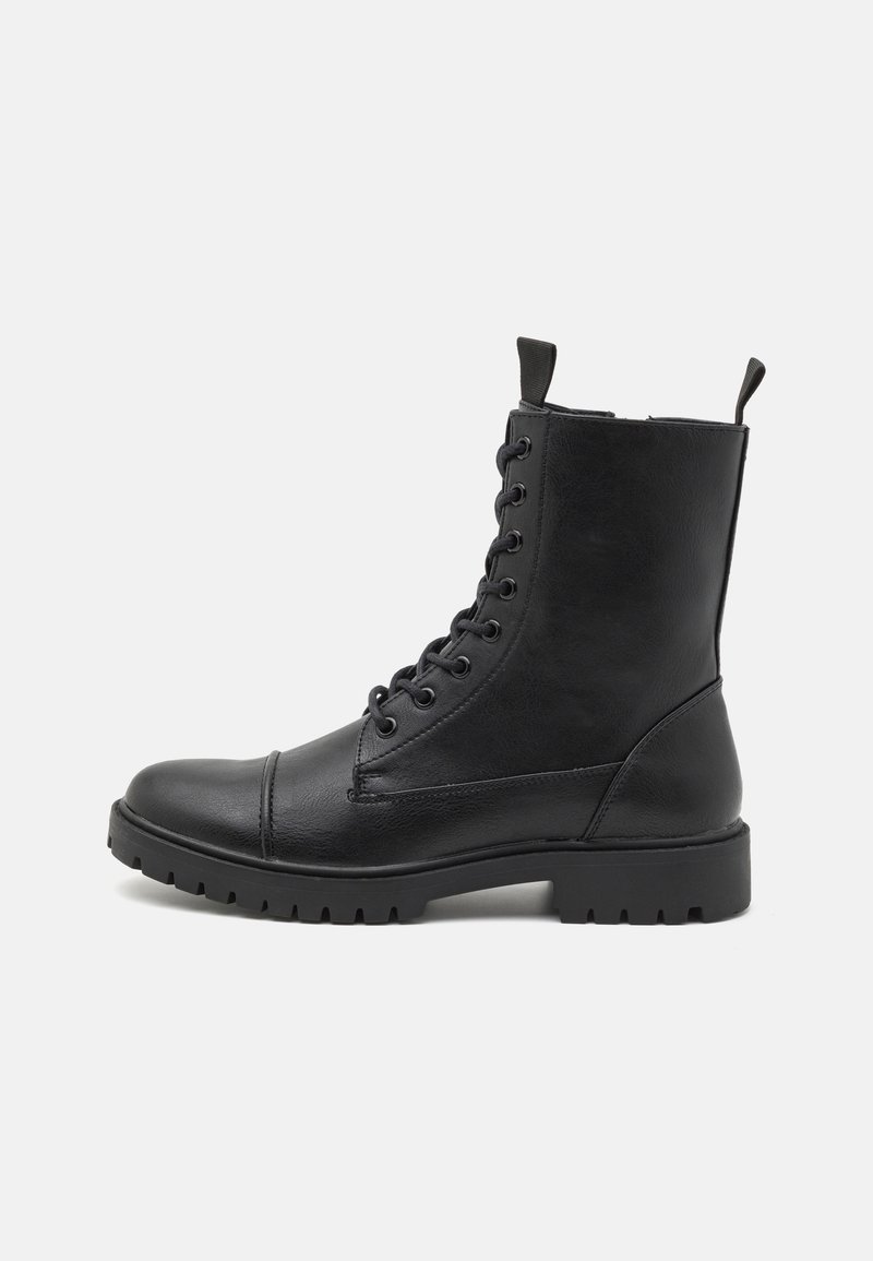 Botte de combat en cuir noir avec laçage à l’avant, languettes en haut et semelle épaisse texturée, vue de côté sur fond blanc.