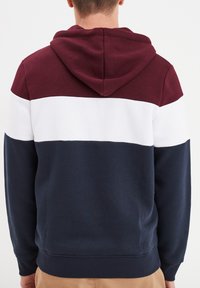Felpa con cappuccio caratterizzata da strisce orizzontali bordeaux, bianche e blu navy, realizzata in materiale morbido, con tasca a marsupio e polsini a costine.