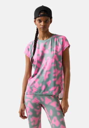 Vrouw draagt een roze en grijs sportshirt met abstract patroon en legging, met een lange vlecht en een zwarte baseballpet achterstevoren.