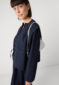 Marineblauw gestreept topje met ronde hals en knoopsluiting, gecombineerd met een kleine zilveren handtas met krokodillenpatroon.