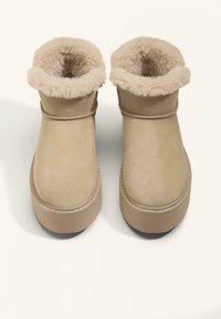 Bruna ankelstövlar med en mockautsida och en mjuk, fluffig pälsfoder runt den övre kanten. Har en rund tå och en tjock, slät sula.