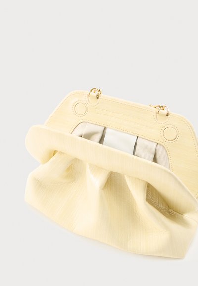 Κρεμ τσαντάκι φάκελος με απαλή υφή, χρυσά μεταλλικά στοιχεία και λεπτομέρειες από πιεσμένο ύφασμα στο εσωτερικό, τοποθετημένο σε απλό ανοιχτό φόντο.