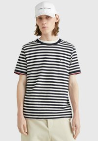 T-shirt a maniche corte a righe navy e bianche con scollo tondo, dotato di un piccolo logo sul petto e accenti rossi a contrasto sulle maniche.