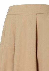 Jupe beige avec une taille plate, plis allant de la taille à l'ourlet, faite de tissu doux, avec une texture lisse.