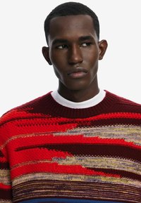 Roter und maroonfarbener gestrickter Pullover mit mehrfarbigen horizontalen Streifen, der über einen gerippten Ausschnitt und ein aufwendiges Texturmuster verfügt.