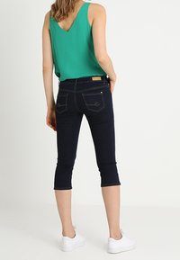 Marineblauwe cropped jeans met een aangesloten ontwerp en achterzakken, gecombineerd met een groen mouwloos topje. Witte sneakers maken de outfit compleet.