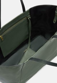 Zielona skórzana torba tote od wewnątrz, z czarną podszewką, zasuwaną kieszonką i złotą okuciami. Gładka tekstura z minimalnymi detalami w designie.