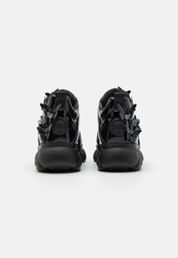 Black patent leather shoes with textured accents, featuring butterfly-shaped details and chunky soles, shown from the back.
