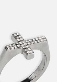 Hõbedane metallrõngas, millel on ristmotiiv. Rist on kaunistatud mitmete selgete rhinestone'idega, mis suurendavad selle visuaalset detaili ja tekstuuri.