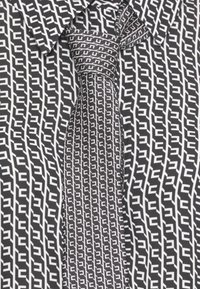 Tessuto a righe bianche e nere con forme geometriche intrecciate, abbinato a una cravatta, che mette in mostra una texture liscia e un design pulito.