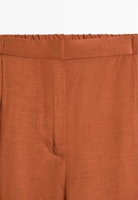 Rustfarvede bukser med høj talje, elastisk linning og skjulte forsideseams, lavet af letvægtsstof.