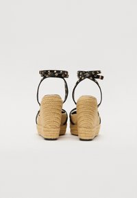 Sandalias de plataforma negras con tacón de yute trenzado. Cuenta con correas al tobillo con acentos circulares dorados y suelas texturizadas.