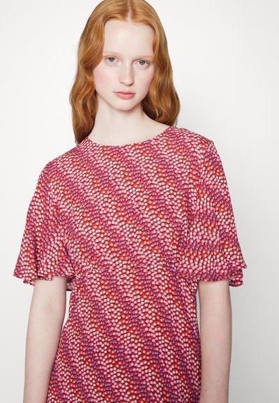 Blusa vermelha com um padrão floral em tons de rosa e roxo. Mangas curtas com volantinho, decote redondo, tecido leve.