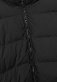 Tissu matelassé noir avec une fermeture éclair courant verticalement au centre, montrant une couture en matelassage et un matériau texturé.