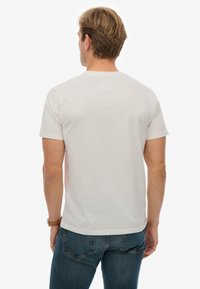 Camiseta de algodón blanca lisa con mangas cortas, escote redondo y un corte relajado, llevada con vaqueros de mezclilla azul oscuro.