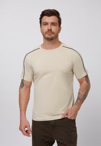 Beige T-Shirt mit kurzen Ärmeln aus weichem Material, mit schwarzen Akzenten an den Schultern und einem Rundhalsausschnitt.