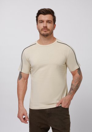 Beige short-sleeve t-shirt made from soft material, featuring black accents along the shoulders and a crew neckline.