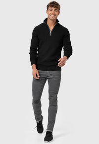 Sort striktrøje med kvart-lynlås krave, parret med tætsiddende grå jeans med teksturerede detaljer og sorte atletiske sneakers.