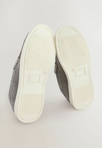 Graue Wildlederschuhe mit weißen Gummisohlen zeigen ein strukturiertes Grip-Muster. Akzente setzen seitliche Nähte für Details.