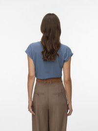 Kvinde med langt brunt hår iført en blå kortærmet bluse stukket ind i højttaljede brune bukser med et brunt bælte, set bagfra.