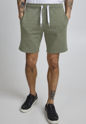  Grønne sweatshorts lavet af blødt stof med elastisk talje, hvid snor og sidelommer. Bæres med sorte sneakers.