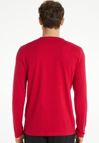 Czerwony longsleeve z gładkiego materiału, z okrągłym dekoltem, luźnym krojem i bez widocznych wzorów czy logo na plecach.