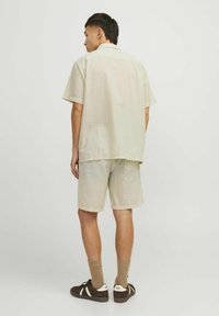 Kortærmet letvægts skjorte og matchende shorts i et lyst beige ternet mønster, parret med brune sko og tan farvede sokker.