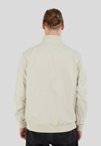 Hellbeige Bomberjacke mit Stehkragen, gerippten Bündchen und elastischem Taillenbund; aus glattem, leichtem Stoff gefertigt.