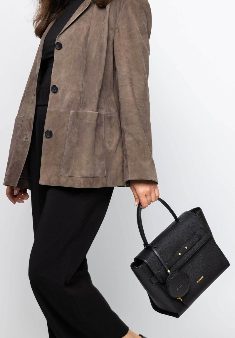 Schwarze Handtasche mit strukturiertem Fischgrätenmuster, goldfarbenen Hardware-Akzenten, runder Reißverschlusslasche und oberen Griffen, kombiniert mit einem braunen Wildleder-Blazer.