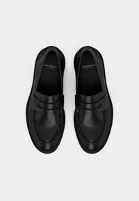 Mocassins en cuir noir avec une finition lisse, un bout arrondi et de subtils détails de couture. Dotés d'une bride à l'avant et d'une semelle texturée.