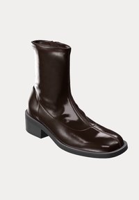 Bruna läderankelboot med en slät, glänsande yta, rund tå och en robust svart klack. Har en dragkedjeslutning på sidan.