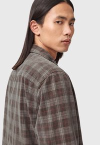 Grau karierte Hemd mit Kragen, aus strukturiertem Stoff, mit roten und schwarzen Linien und einem geknöpften Design, seitlich gezeigt.