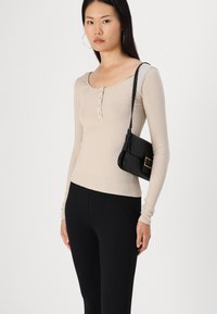 Haut beige à rayures avec des manches longues, un décolleté en cœur et des détails de boutons, associé à un pantalon noir ajusté et un petit sac à main noir.