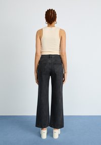 Jeans en denim noirs à taille haute et à pattes larges, avec un design classique à cinq poches et des poches arrière à patch, associés à un top à bretelles ajusté.