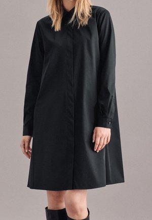 Schwarzes, knöpfbares Kleid mit langen Ärmeln, geradem Schnitt und seitlichen Schlitzen. Mit Kragen und Manschetten mit Knopfakzenten. Glatte Textur.