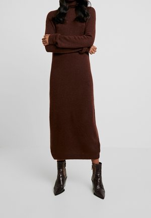 Femme portant une longue robe-pull marron à col roulé avec des manches longues et des bottines marron foncé à bout pointu.