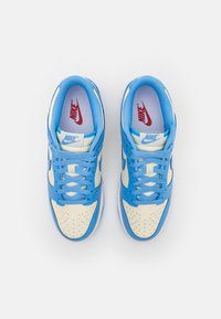 Nike tenisice s svijetloplavom i kremastom bojom, gornji dio od kože, perforirani vrh i plave vezice. Crveni logo na jeziku.