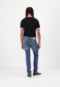 Black short-sleeve T-shirt paired with blue denim jeans featuring a label on the back waist and a slim fit. Worn with black sneakers.
