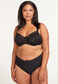 Black lace bra with underwire, featuring a sheer panel and decorative stitching. Paired with high-waisted black briefs, smooth fabric.