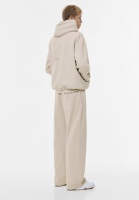 Beige Kapuzenpullover und weite Sweatpants aus weichem Material. Der Hoodie verfügt über eine Kängurutasche und minimalistische Stickereien.