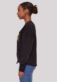 Schwarzer Sweatshirt mit floralem Stickmuster auf der Vorderseite, mit Rundhalsausschnitt, überschnittenen Schultern und lockerer Passform. Getragen mit blauen Jeans.