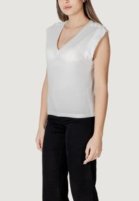Top bianco senza maniche con scollatura a V, caratterizzato da dettagli con bottoni sulle spalle. Realizzato in tessuto morbido, ha una vestibilità aderente e un design semplice.