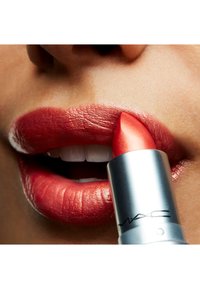Rode lippenstift met metalen glans aangebracht op zachte, volle lippen. De tube is zilver met een kenmerkend MAC-logo. Glad van textuur, levendige kleur.