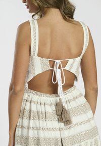 Top blanco y beis con estampado, con un respaldo cuadrado, atado con un hilo blanco, que presenta una tela texturizada y borlas decorativas.