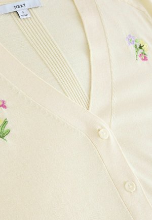 Cremefarbener Cardigan mit V-Ausschnitt, verziert mit floralen Stickereien in Rosa, Gelb und Grün. Weicher Stoff; mit Knopfverschluss und gerippten Details.