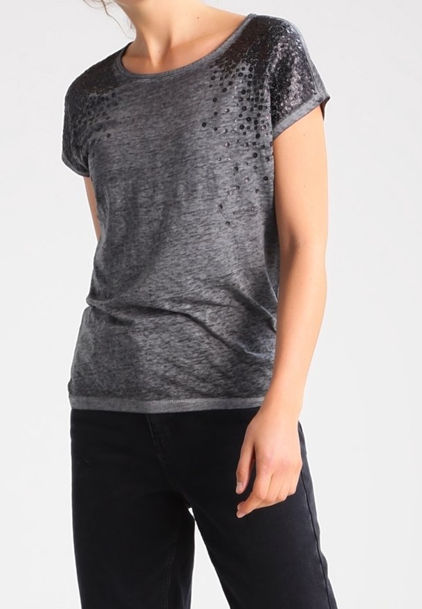 Femme portant un haut court en velours gris foncé avec des embellissements en sequins sur les épaules, associé à un pantalon noir.
