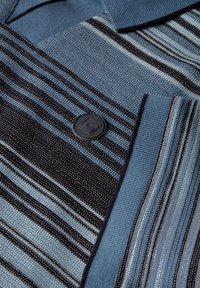 Pruhované polo tričko v modré a černé barvě, které se vyznačuje texturovanou tkaninou, černým knoflíkem s geometrickým vzorem a kontrastním límcem.