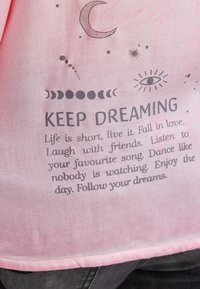 Rosa Stoff mit schwarzem Text und Illustrationen, einschließlich Mondphasen, Halbmond, Stern und Auge, das eine inspirierende Botschaft über das Leben und Träume vermittelt.