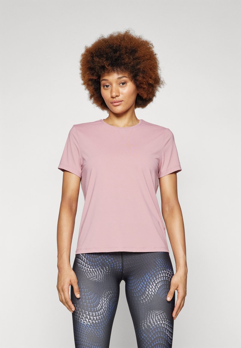 Light pink short-sleeve athletic t-shirt with a round neckline. Soft, stretchy fabric. Worn with patterned dark leggings featuring blue accents.